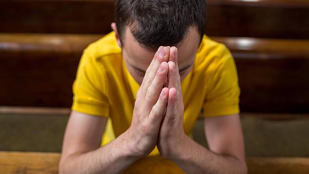Junger Mann betet in einer Kirche, Symbolfoto