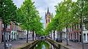 Delt-Kanal mit alten Häusern, Fahrrädern und Autos und dem alten Kirchturm der Oude Kerk, Delft, Niederlande
