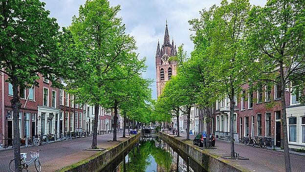 Delt-Kanal mit alten Häusern, Fahrrädern und Autos und dem alten Kirchturm der Oude Kerk, Delft, Niederlande