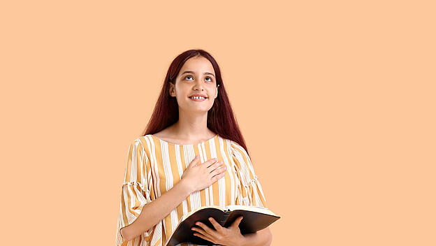 Teenage girl with Holy Bible on beige background