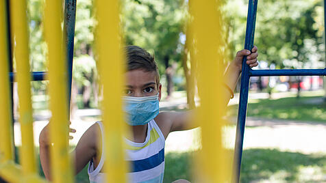 Kind mit Maske auf Spielplatz
