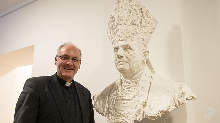Bischof Rudolf Voderholzer steht neben einer Büste von Papst Benedikt XVI.
