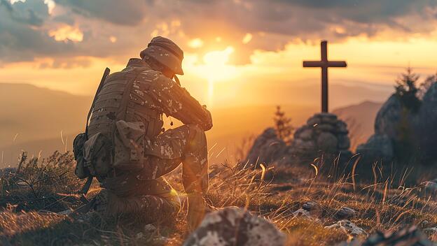 Ein Soldat kniet bei Sonnenuntergang vor einem Kreuz.