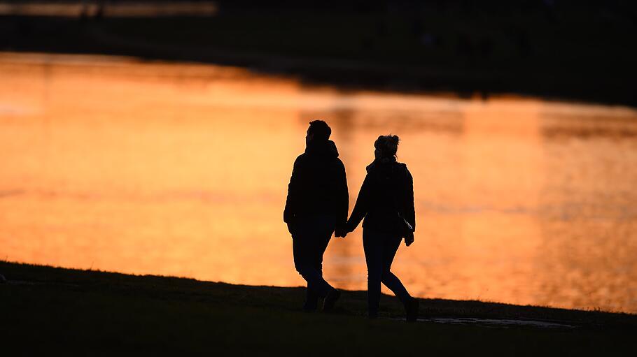 Zwei Menschen zeichnen sich bei Sonnenuntergang am Ufer der Elbe als Silhouette ab.