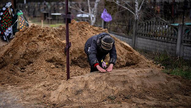 Butscha: Eine alte Frau legt Blumen auf das Grab ihres Mannes