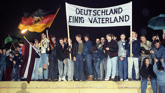 Auf der Mauerkrone feiern Deutsche aus Ost und West 1990 die Wiedervereinigung