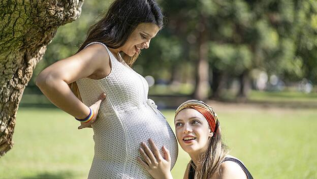 Lateinamerikanerin hört dem Bauch seiner schönen schwangeren Freundin zu Latin woman listening to his beautiful pregnant
