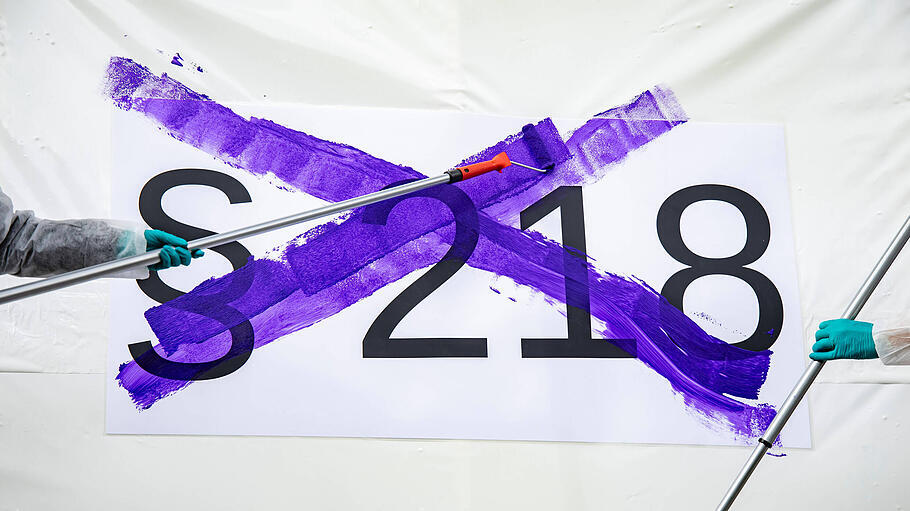 Aktivistinnen streichen symbolisch mit lila Farbe die Schrift § 218 bei einer Kundgebung für die Abschaffung des Paragraphen 218.