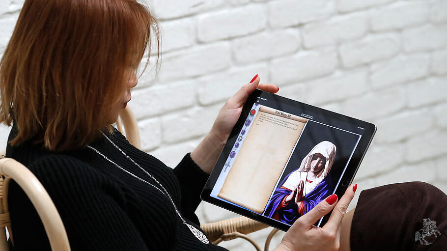 Woman praying the Rosary on a digital tablet Ipad.