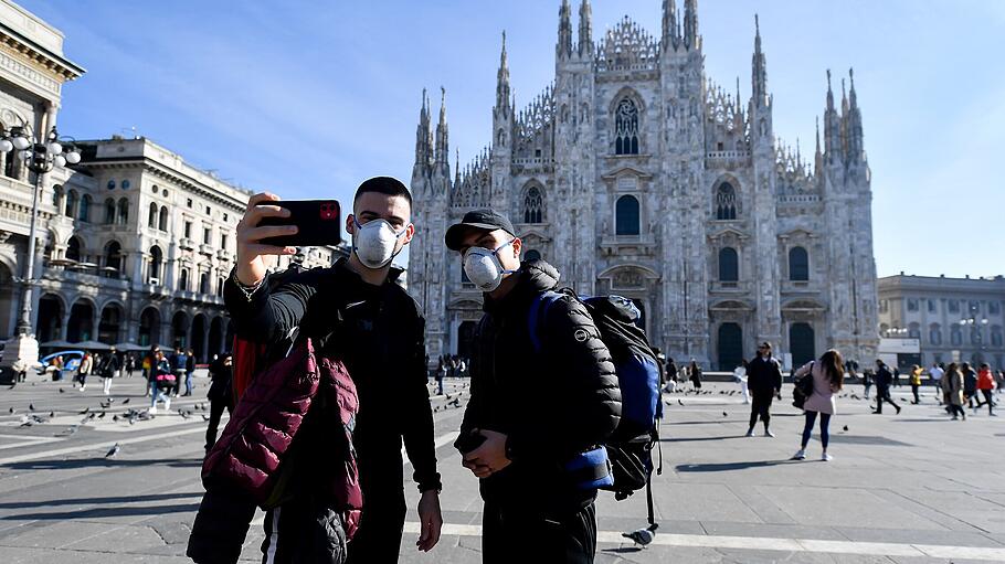 Touristen fotografieren sich mit Mundschutz vor dem Mailänder Dom.