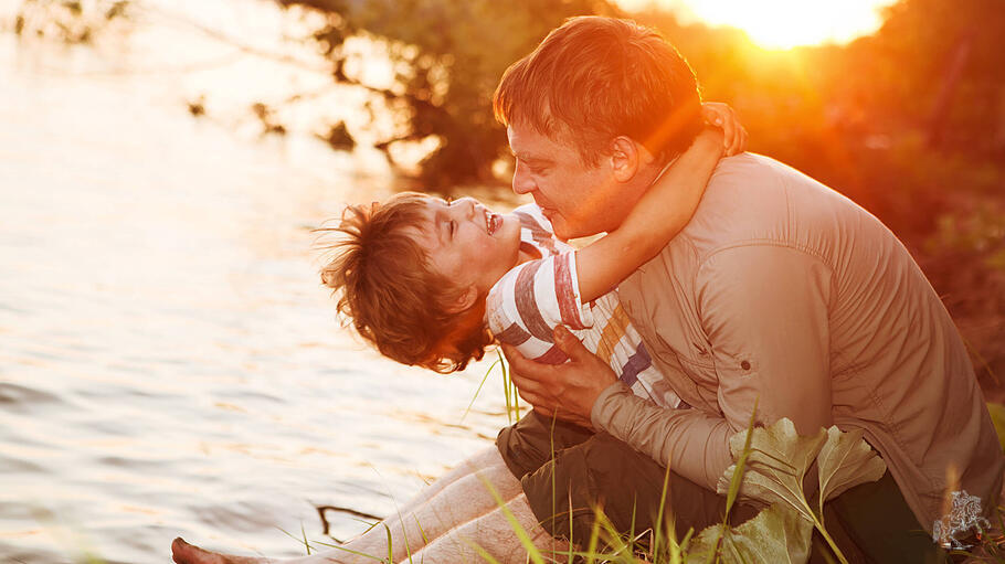Gl&uuml;cklicher Vater und Sohn spielen bei Sonnenuntergang am Fluss.